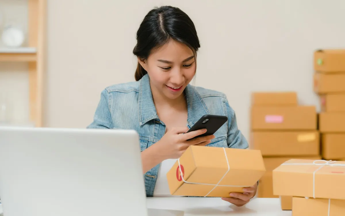 Emprendedora revisa productos y cajas de pedidos junto a su computador