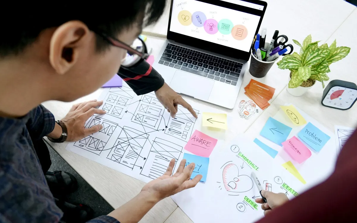 Diseñador organiza wireframes de un sitio web frente a su computador