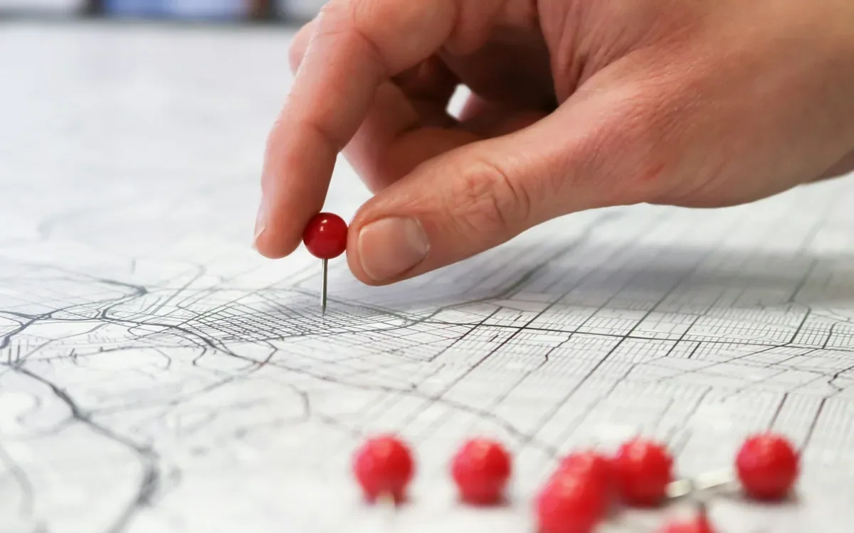 Mano marca una ubicación en un mapa de calles con un pin rojo