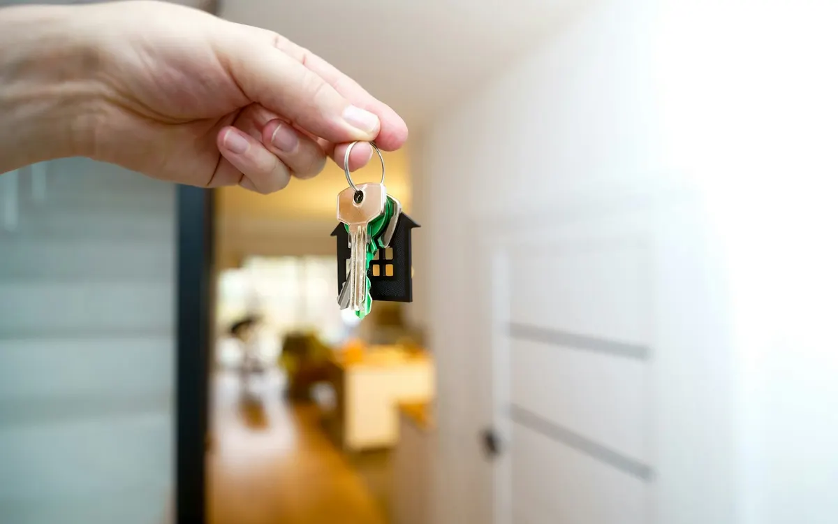 Mano sostiene las llaves de una vivienda junto a la puerta de entrada