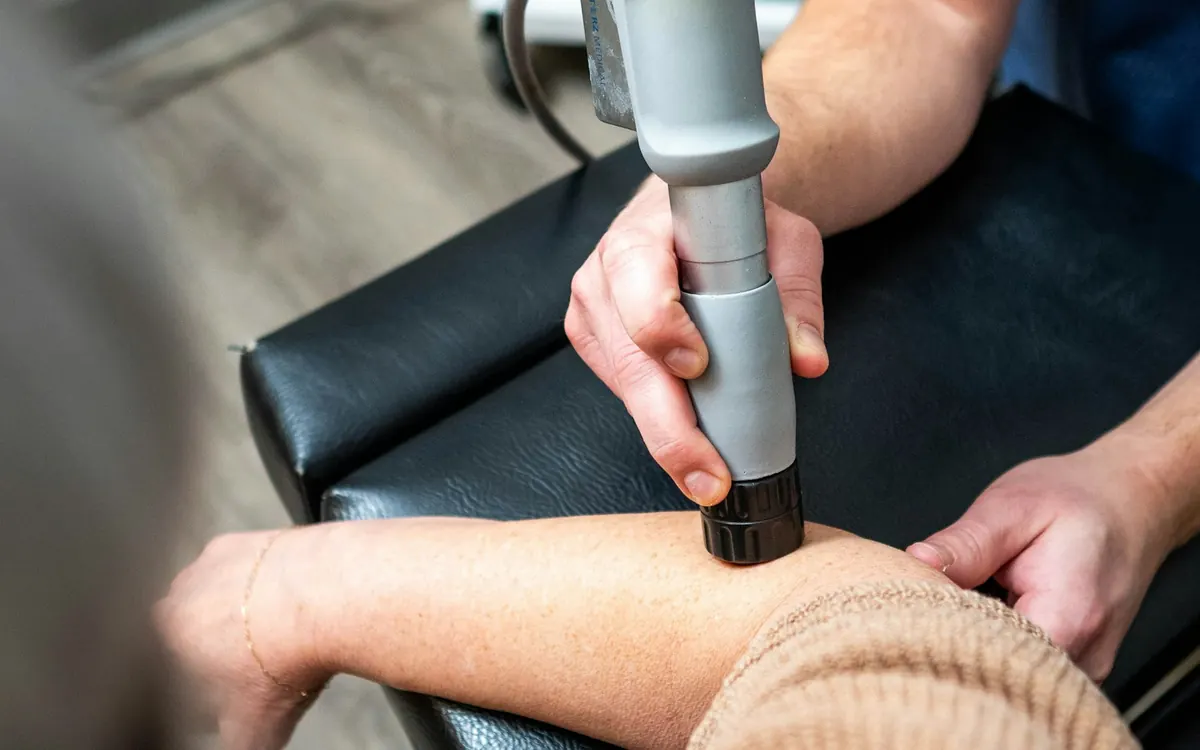 Kinesiólogo aplica terapia de ondas de choque en el codo de una paciente